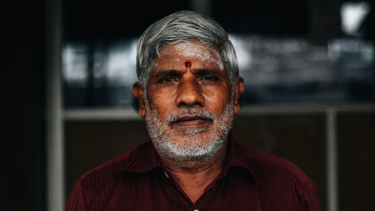 Close-up portrait of an elderly man with facial expressions and cultural marks.