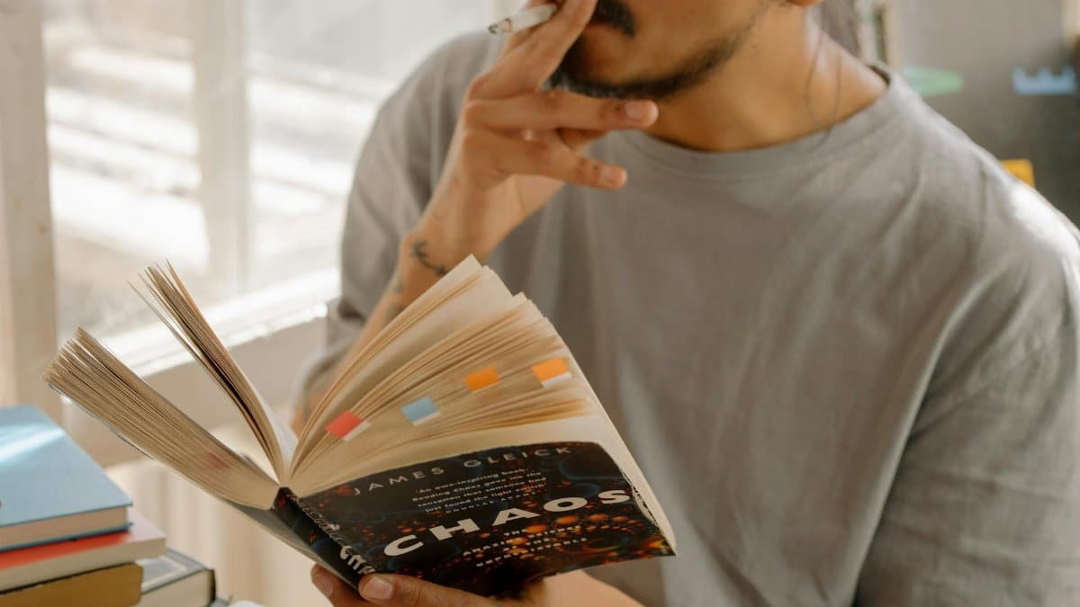 A man reads a book titled 'Chaos' while smoking indoors, creating a relaxed atmosphere.