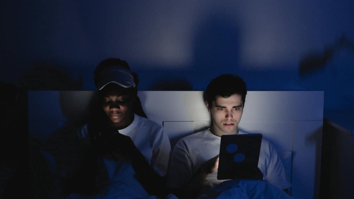 A couple sitting in bed, illuminated by mobile devices, creating a moody and dramatic atmosphere.
