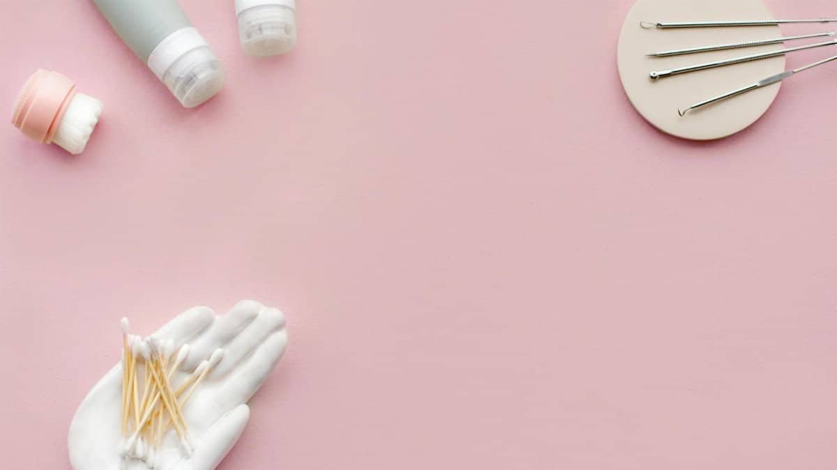 Collection of skincare tools and products arranged on a pastel pink surface in a flat lay style.
