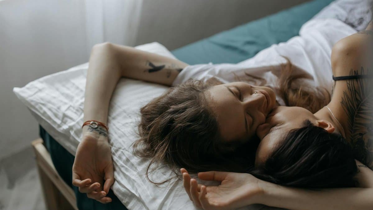 Two women intimately embracing on a bed, capturing love and affection.
