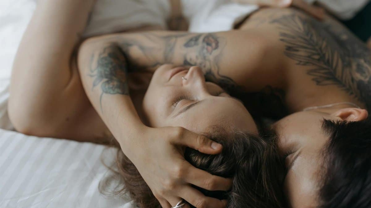 Close-up of a loving couple embracing in an intimate moment on a bed, showcasing tattoos and affection.