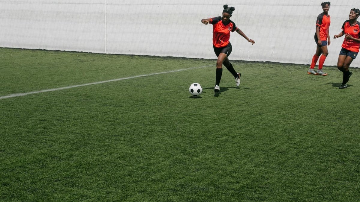 Young African American females playing in football on sports ground in sunny day
