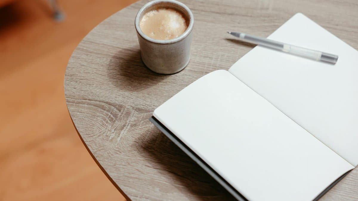 Open notebook with blank pages and coffee on a wooden table, ideal for creativity.