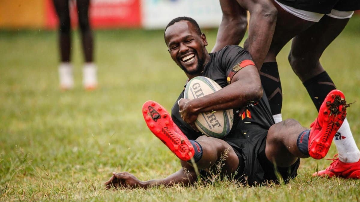 Smiling rugby player celebrating a successful try on a grassy outdoor field.