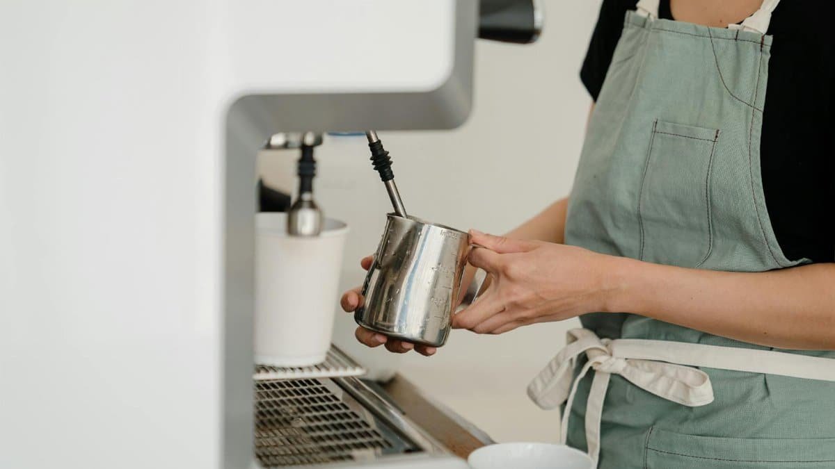 A barista in an apron prepares fresh espresso in a modern café setting.