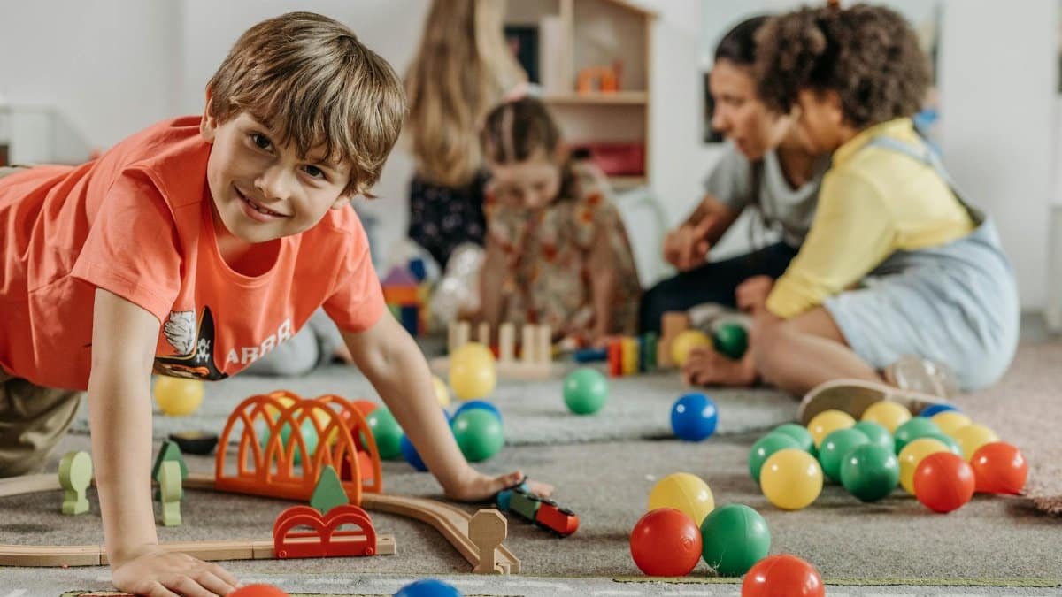 Happy children and a caregiver playing with colorful toys in a lively indoor playroom setting.