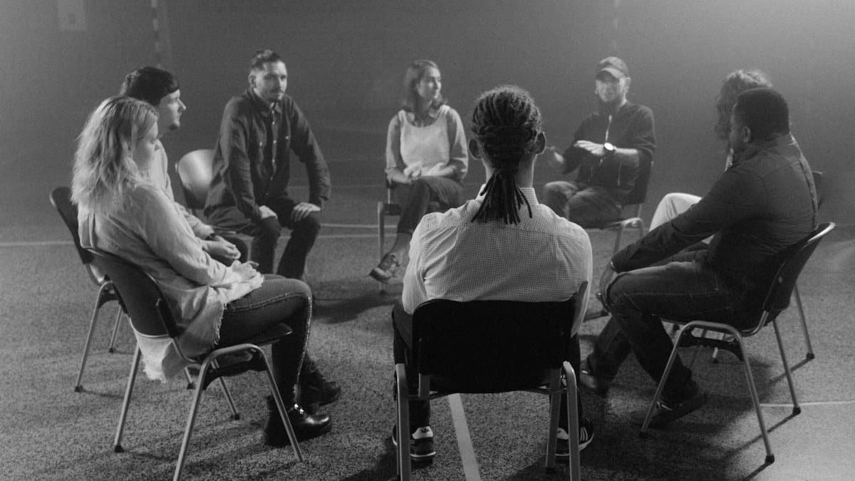 A diverse group of people in a circle discussing and supporting each other in a therapy session.