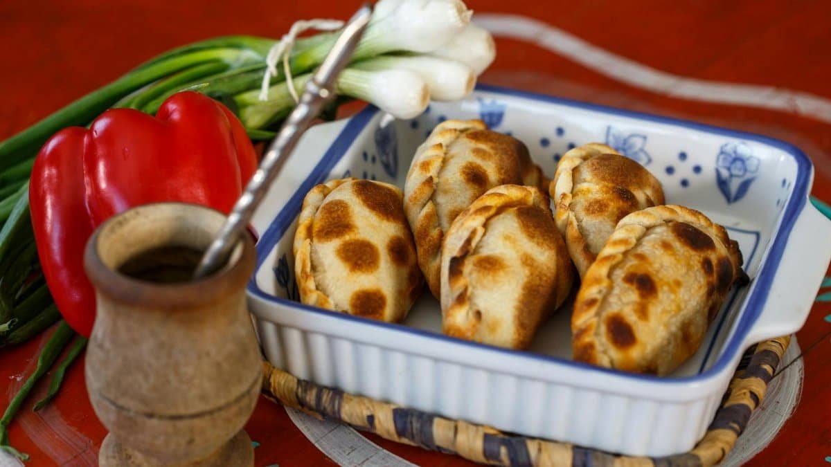 Baked empanadas in a dish with fresh vegetables on a vibrant table.