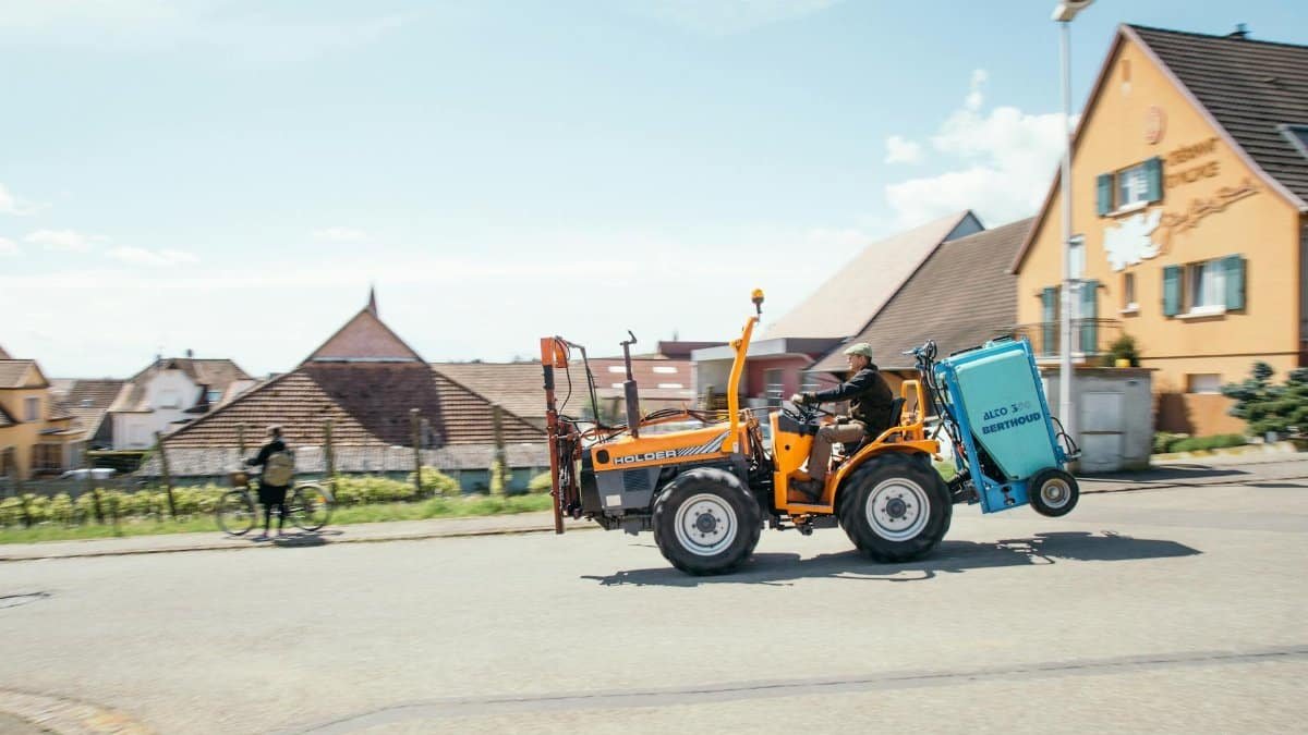 A tractor driving through a village street with traditional houses in the background.
