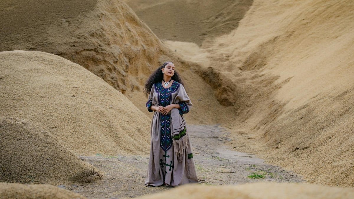 A woman in traditional Ethiopian dress stands amidst rolling sand dunes, showcasing cultural heritage.