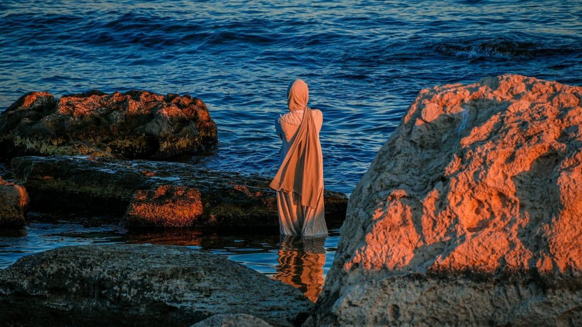 A woman in traditional clothing stands alone at the rocky shore of the Caspian Sea in Aktau, Kazakhstan.