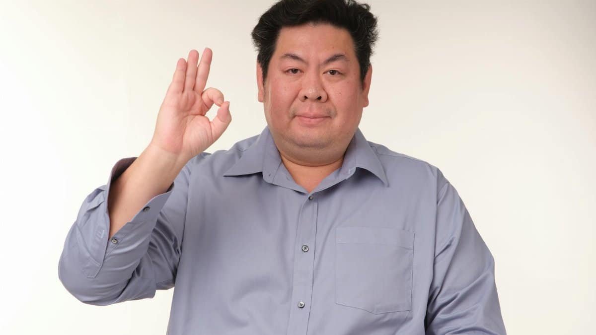 A man in a blue shirt making an 'ok' gesture against a neutral background, creating a calm and positive vibe.