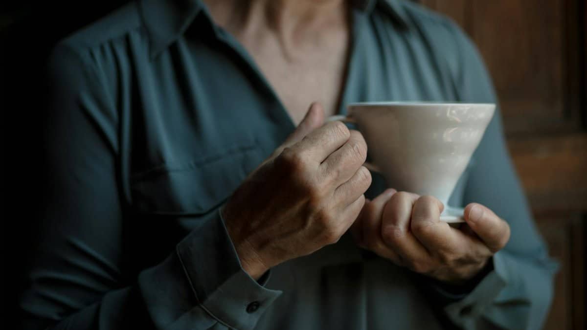 A serene close-up of a person holding a white ceramic coffee cup indoors.