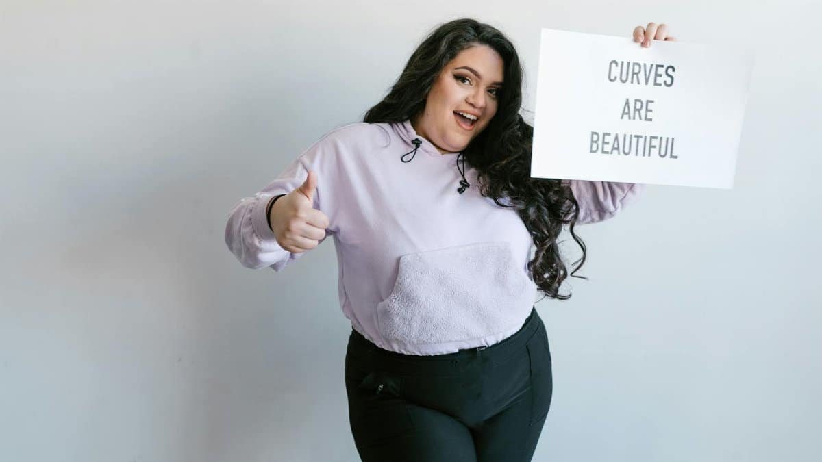 Cheerful plus-size woman holding sign 'Curves Are Beautiful,' promoting self-love.