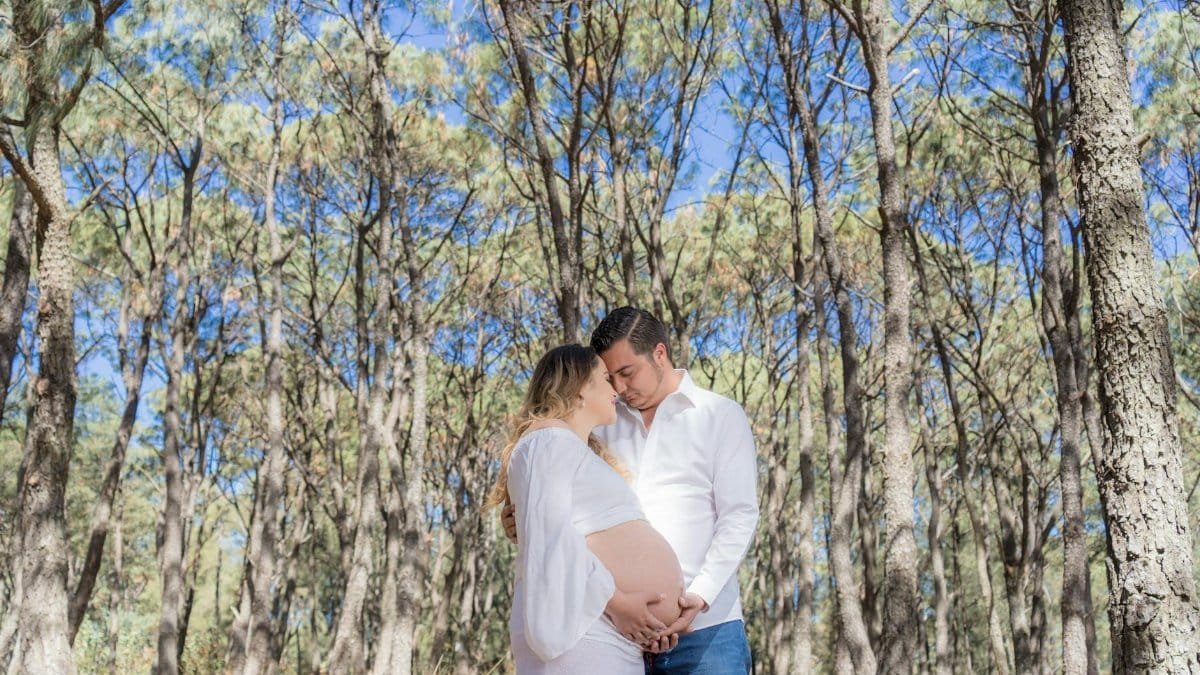 A peaceful outdoor portrait of a couple embracing, highlighting the woman's baby bump in a serene forest.
