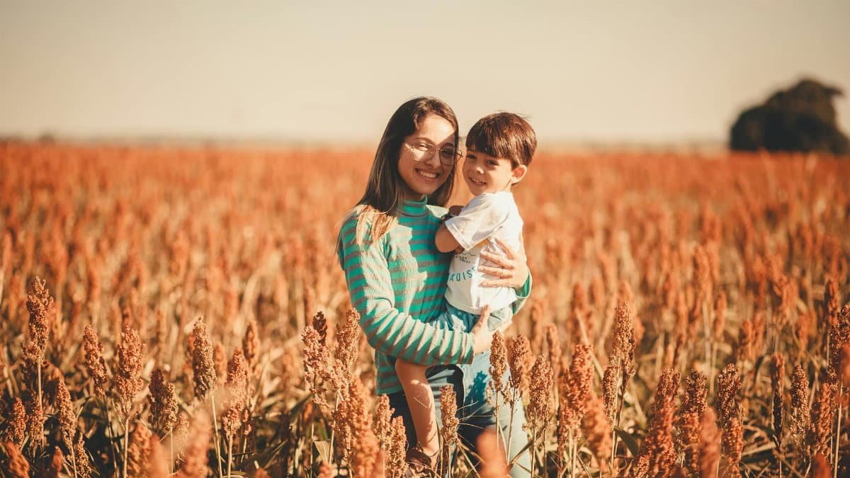 Smiling mother and son embracing in a tranquil sorghum field during summer sunset.