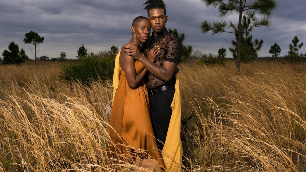 A stylish couple embracing in a grassy field during twilight, showcasing modern fashion.