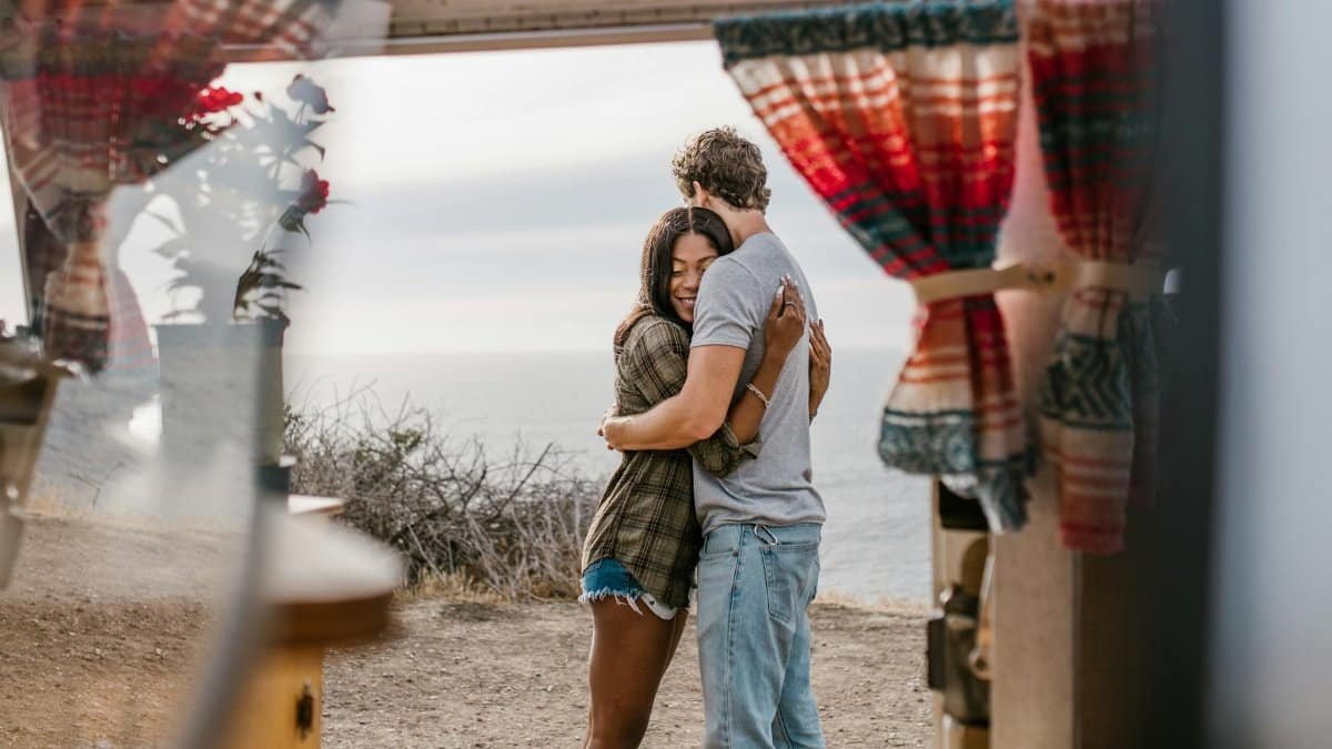 A loving couple embracing near a seaside view seen through a window, evoking warmth and romance.