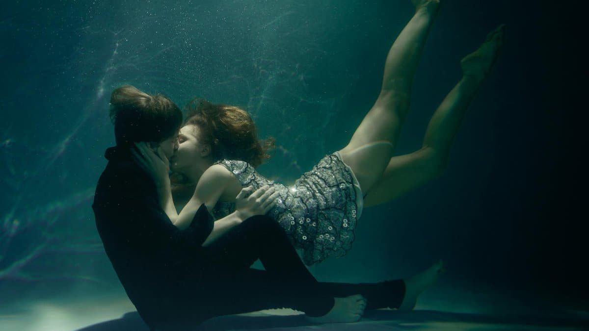 Couple embracing and kissing underwater in an artistic scene.