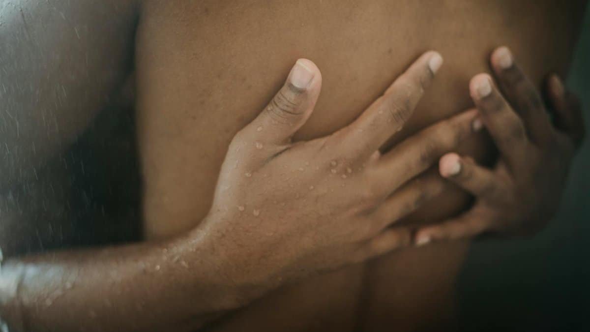 Close-up of two men embracing warmly under running water, showcasing intimacy and connection.