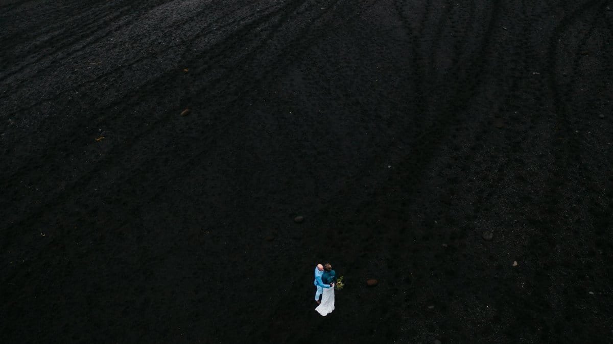 Drone shot of a couple embracing on Iceland's volcanic black sand beach in Vik, Mýrdalshreppur, highlighting romance and nature.