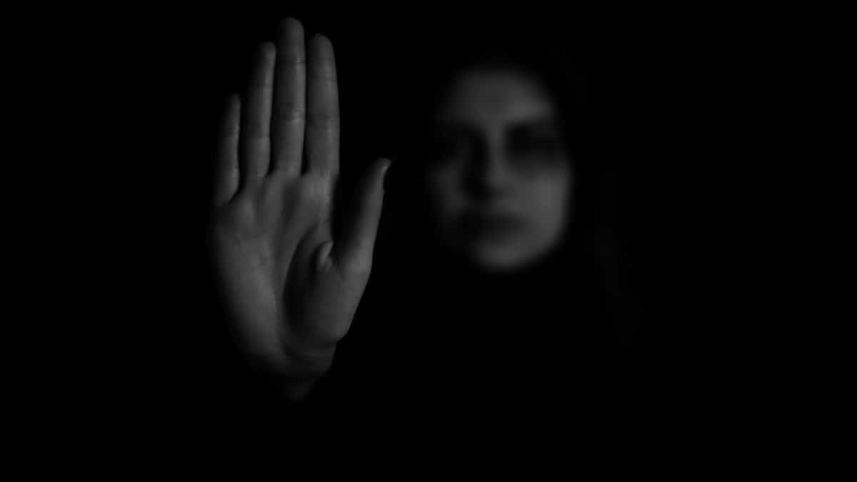 A grayscale photo of a hand showing a stop gesture with a blurred face in the background.