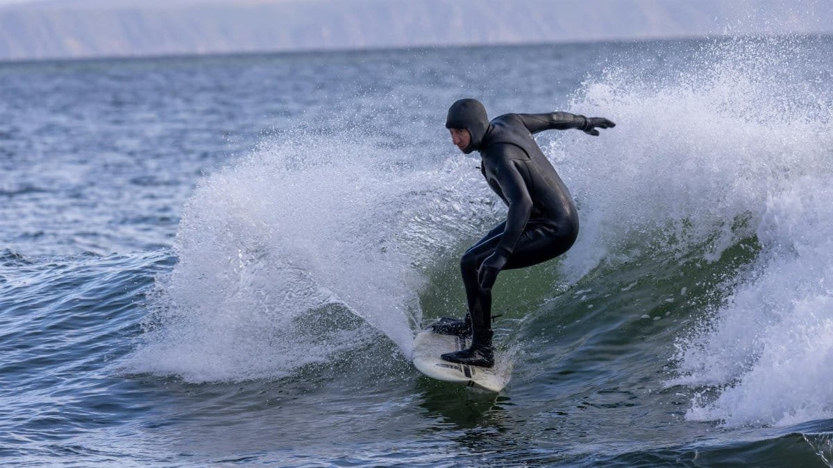 Surfer in wetsuit skillfully rides a wave on a cold day, showcasing expert technique.