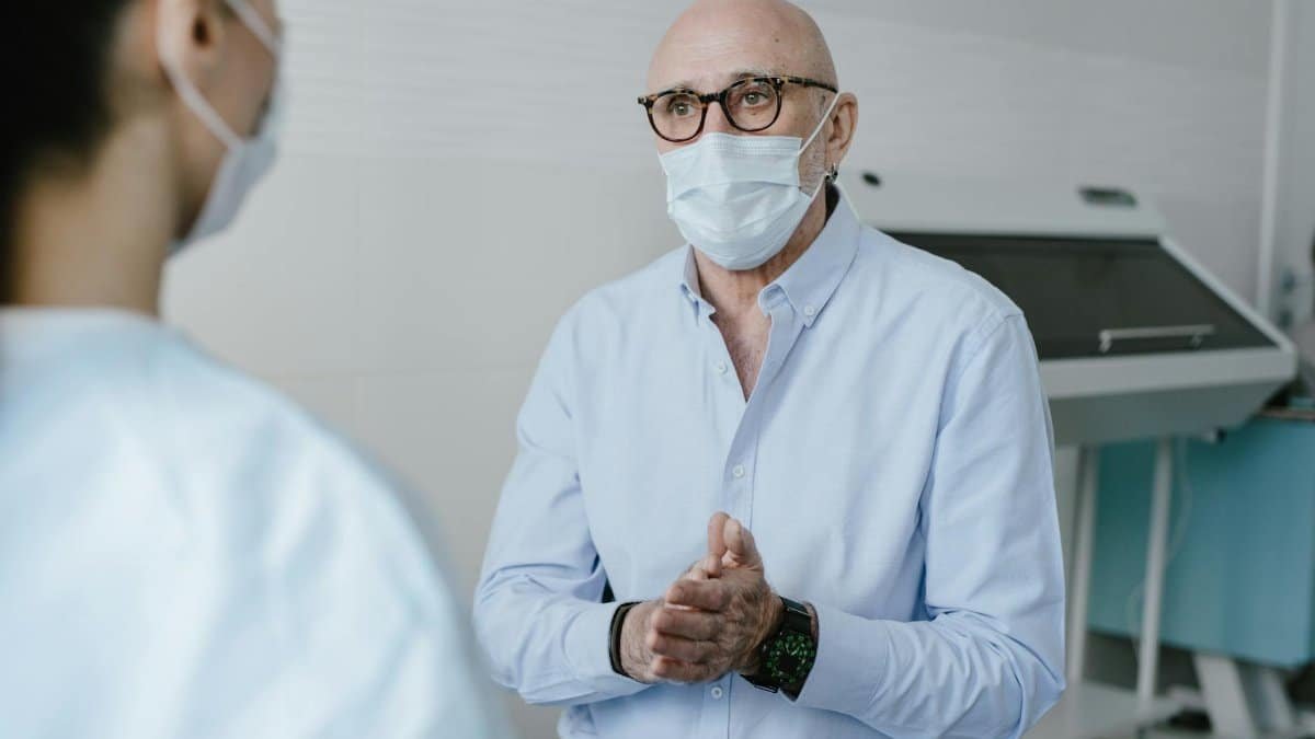 Masked bald doctor in conversation with patient, focus on new normal healthcare.