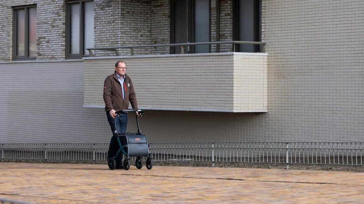 Elderly man using a rollator on urban street, outdoor setting in daylight.
