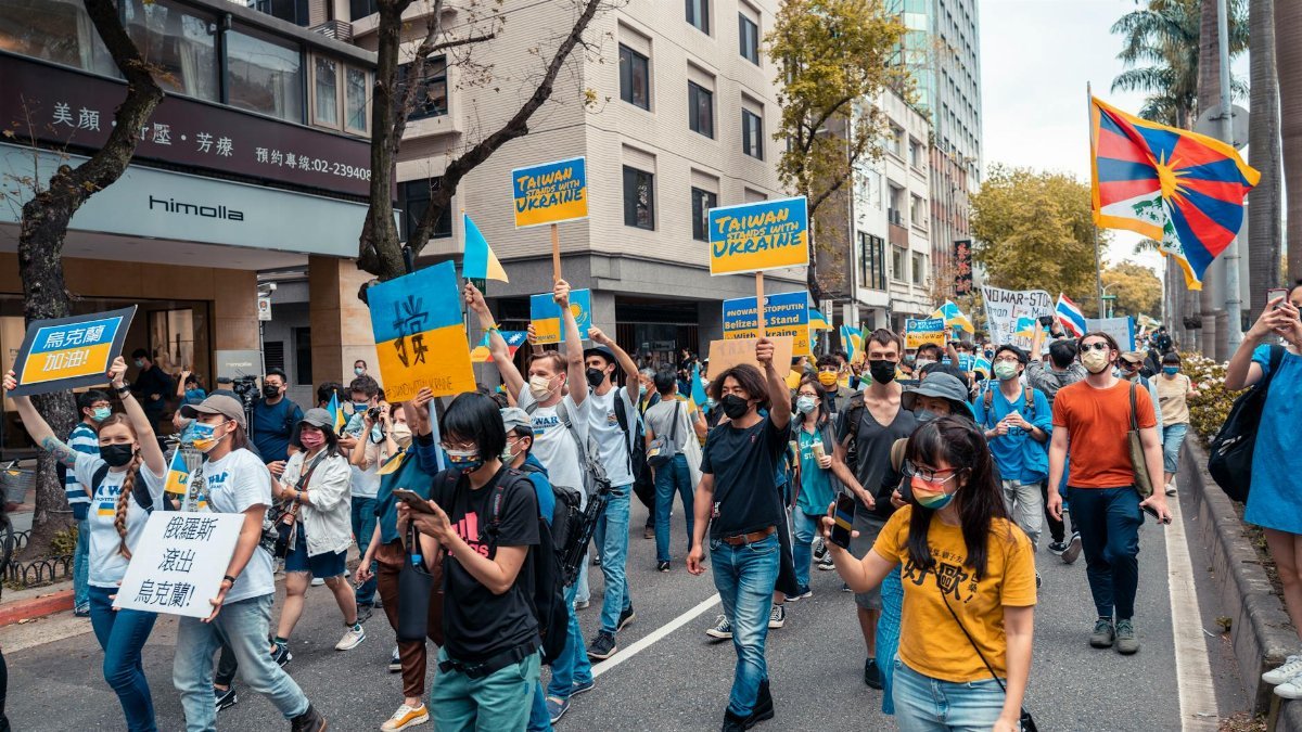 Crowd of people at a street protest with flags and signs supporting Ukraine and Taiwan.