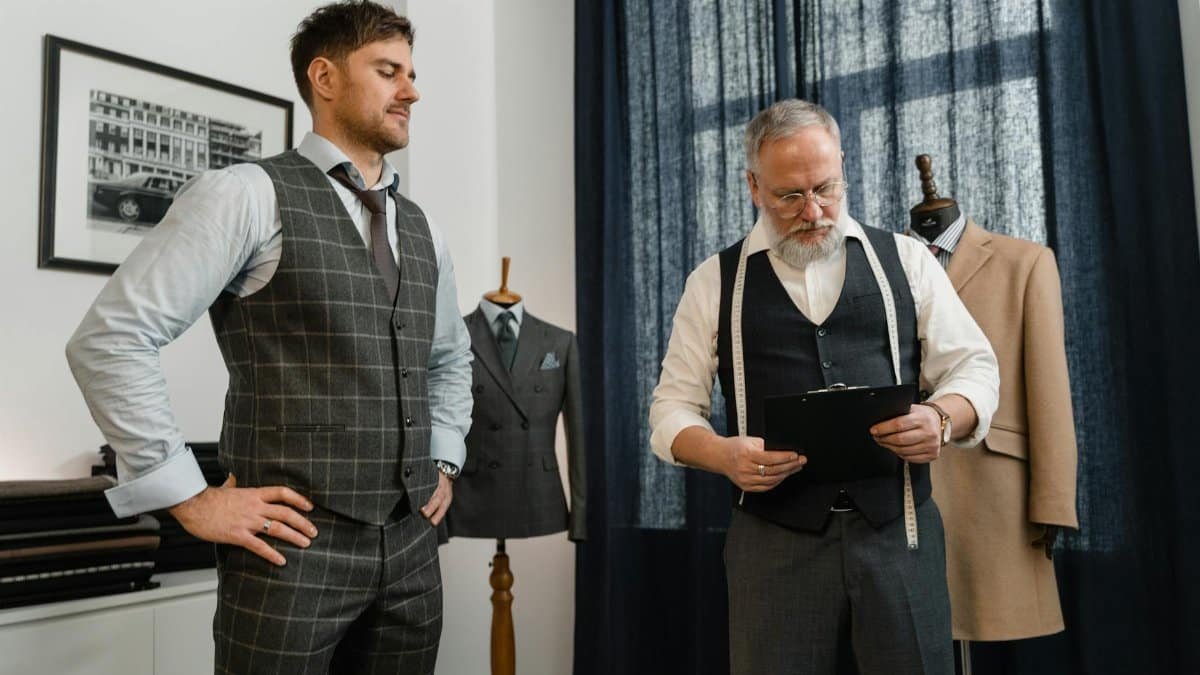 Tailor fitting a bespoke suit for a client in a modern fashion workshop setting.