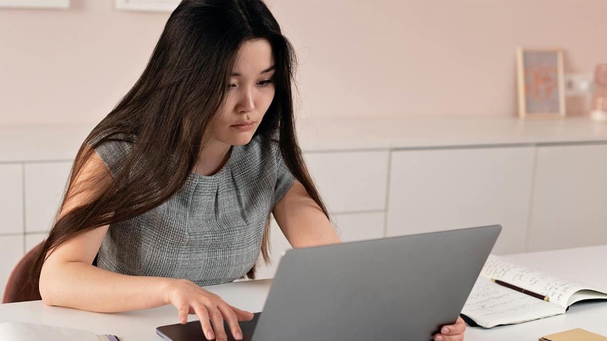 Asian woman in a modern office setting working on a laptop, symbolizing entrepreneurship and professionalism.