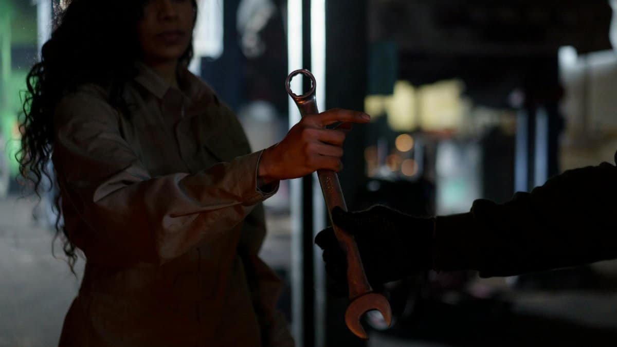 A mechanic handing over a wrench in a dimly lit garage workshop, creating a moody atmosphere.