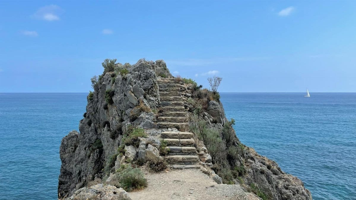 Beautiful rocky cliff with steps overlooking blue sea near Finale Ligure, Italy.