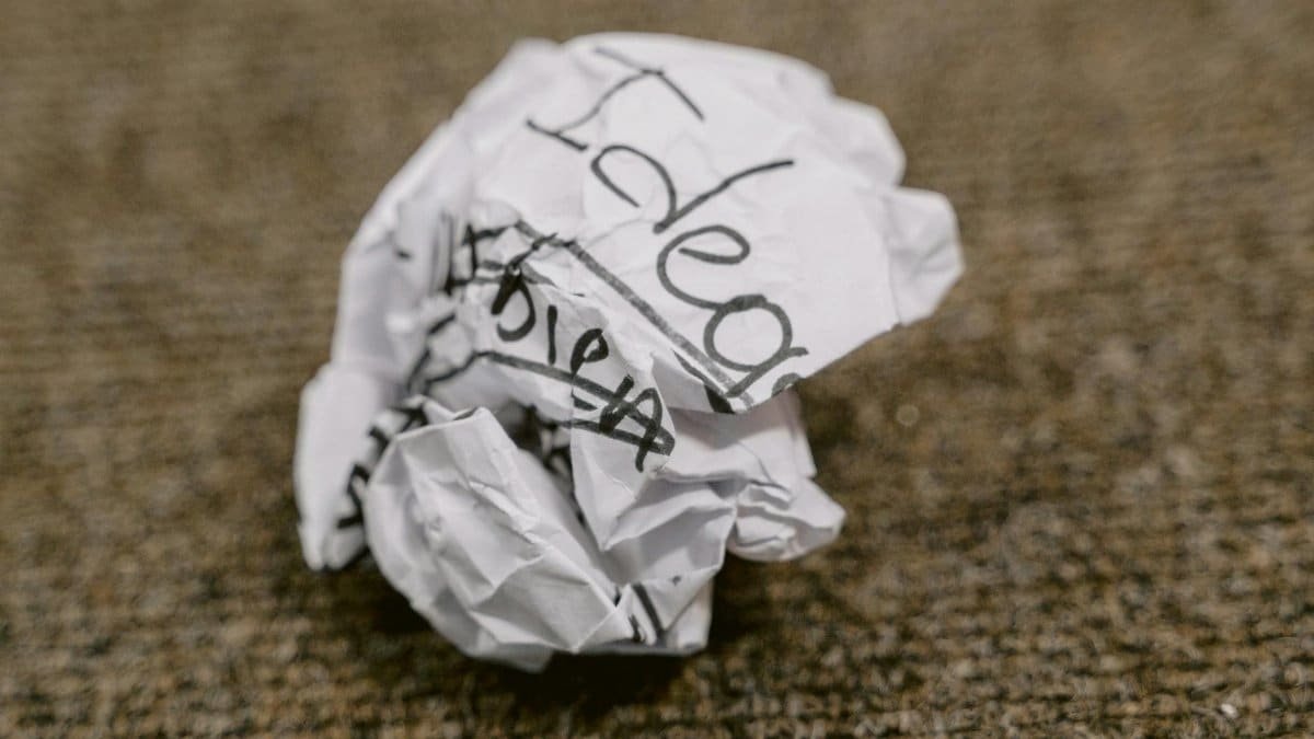 Close-up of a crumpled paper ball with 'Ideas' written on it, symbolizing discarded thoughts.