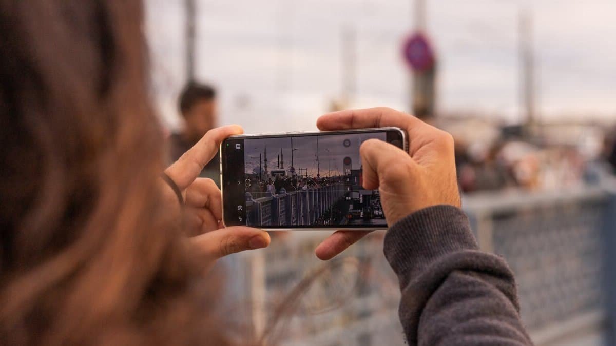 A person photographing İstanbul's skyline at sunset from a bridge, capturing urban life.