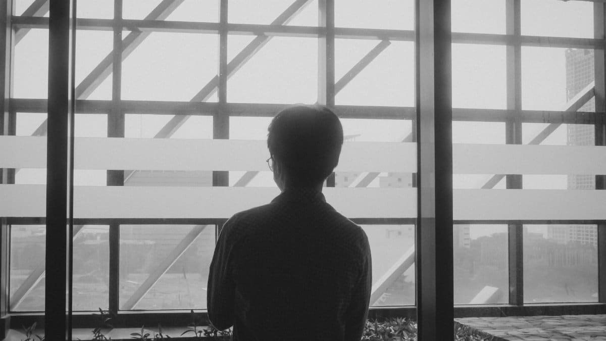 Black and white silhouette of a man gazing out of a modern glass window