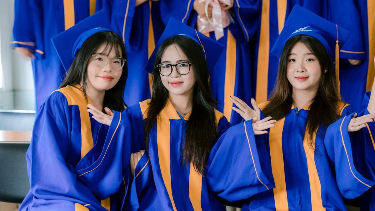 Three graduates in blue gowns celebrating their achievement indoors.