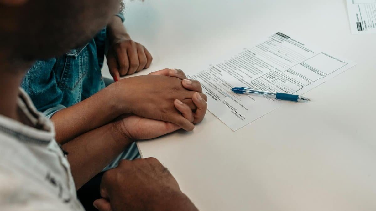 A family supports each other during an adoption process, holding hands over important documents.