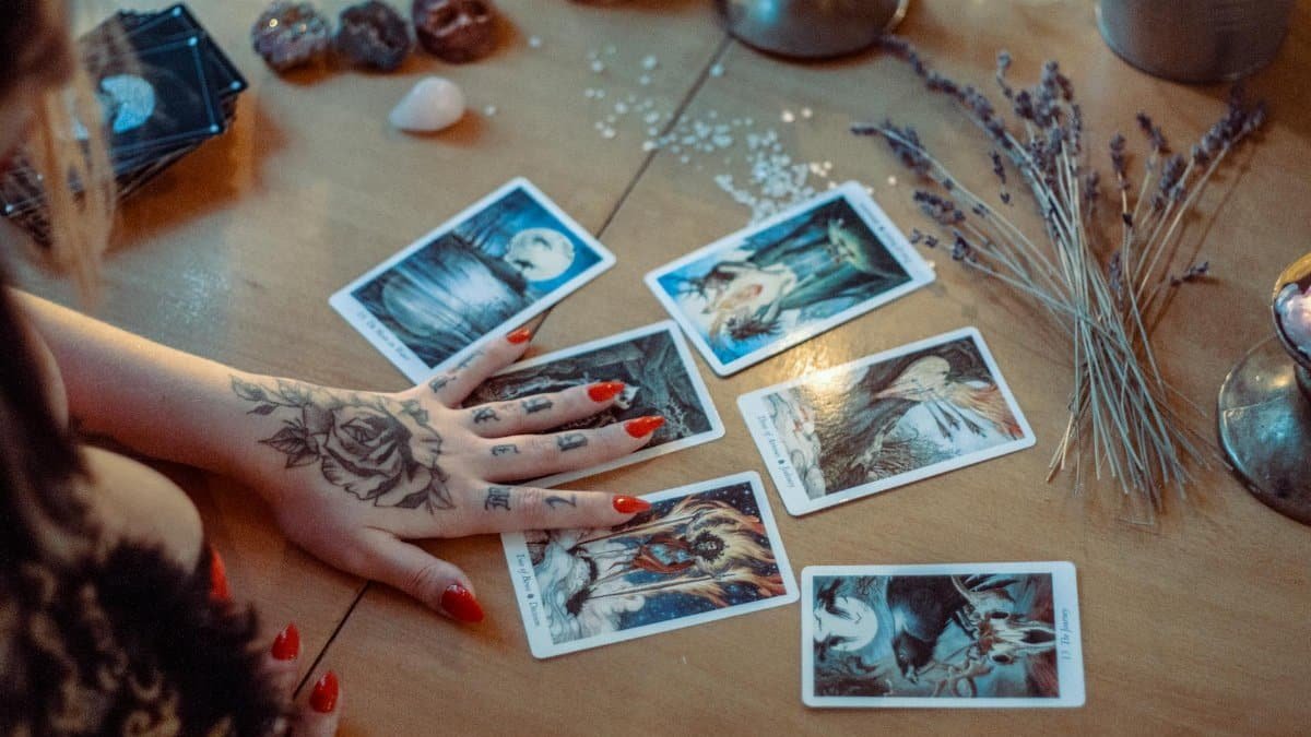 A mystical setup featuring tarot card reading on a wooden table, with artistic tattoos and dried flowers.