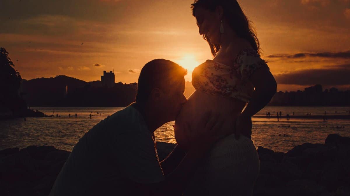 Silhouette of a loving couple at the beach during sunset, embracing pregnancy.