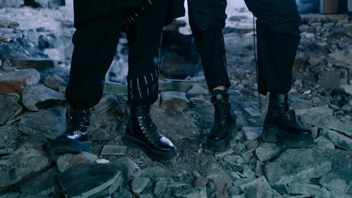 Two people wearing stylish black boots in a gritty urban ruin setting.
