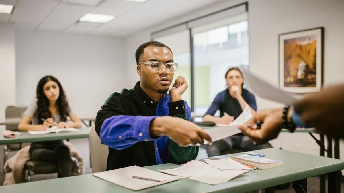 College students sitting in a classroom receiving papers, focused on studies and assignments.