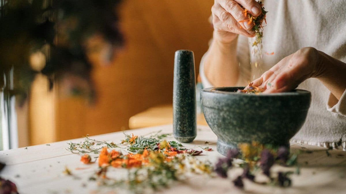 Close-up of hands grinding herbs and flowers in a mortar for natural remedies.