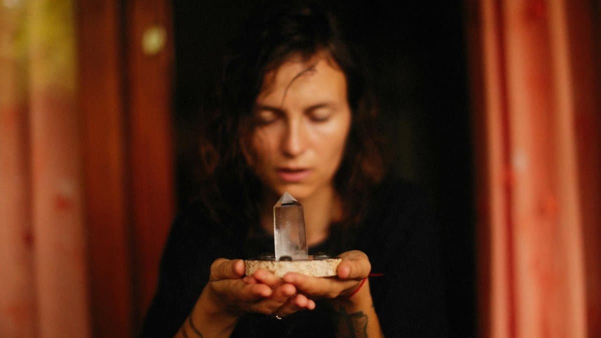 A woman meditates with a healing crystal held in her hands inside a warm, cozy room.