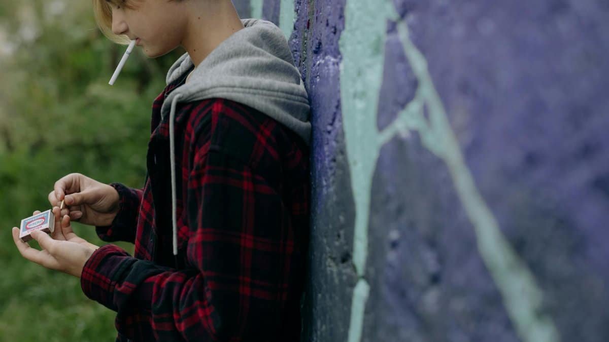 Teenager smoking a cigarette against a graffiti wall, representing rebellion.