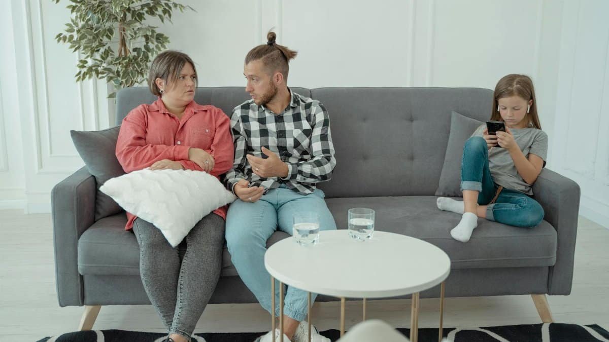 A family therapy session with parents discussing things while a child is absorbed in her smartphone.