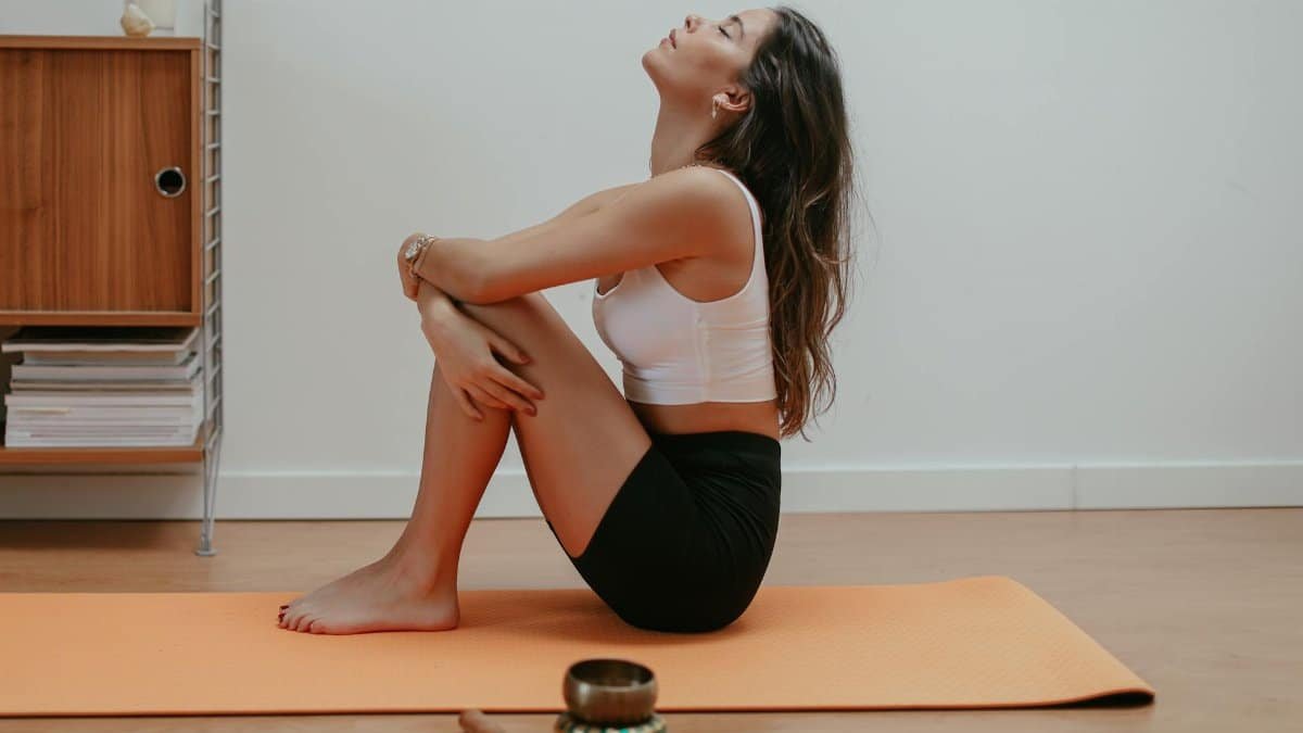 Woman meditating on orange yoga mat indoors, emphasizing relaxation and mindfulness.