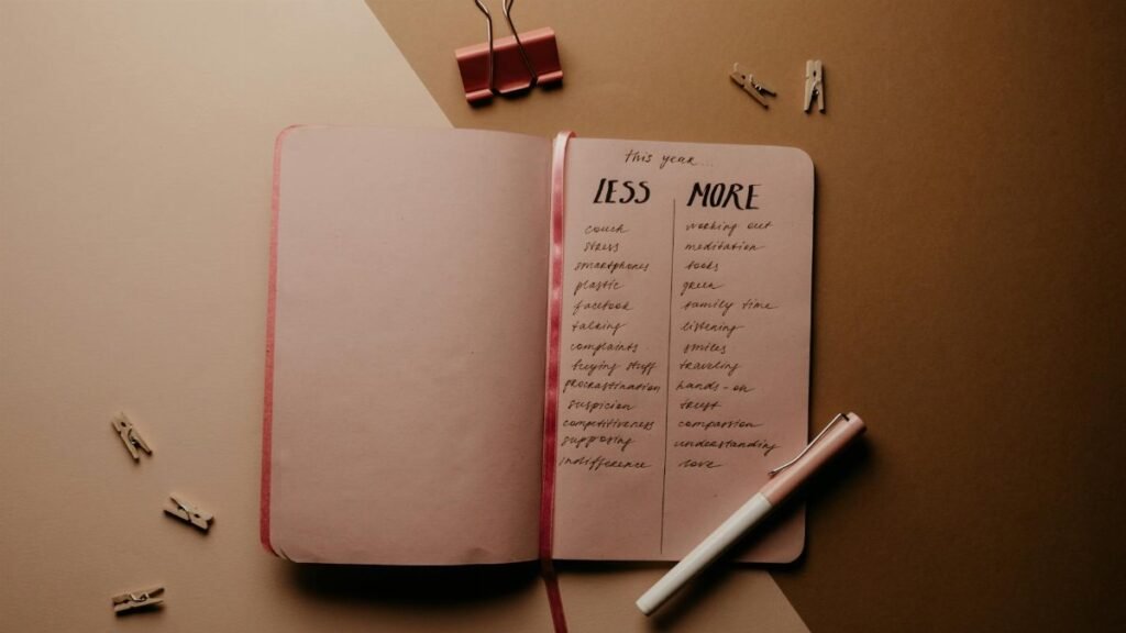 Open notebook with a list of goals under 'Less' and 'More', pen beside it, on a brown background.